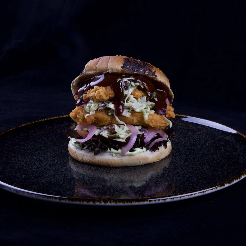 Burger mit Crunchy Chicken Burger Patty, Korean BBQ Sauce, Wasabi-Spitzkohl, Pink Onions, Lollo Rosso und gerösteten Erdnüssen