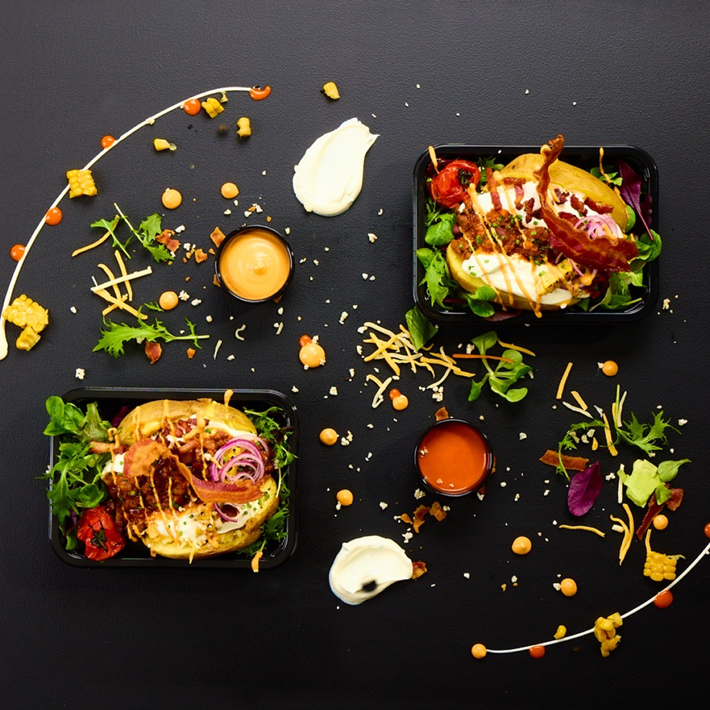 Aufgeschnittene Backkartoffel gefüllt mit Sour Cream und Bolognese, belegt mit krossem Bacon und einem Streifen Mexican Chipotle Dip, garniert mit frischen Schnittlauch-Ringen